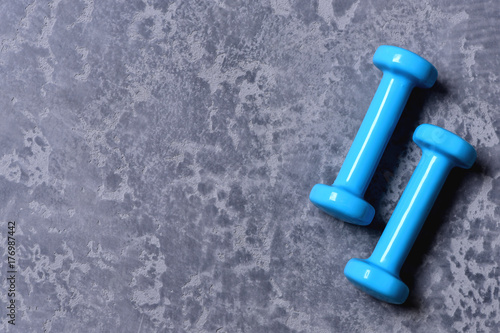 Dumbbells made of cyan blue plastic on grey texture background