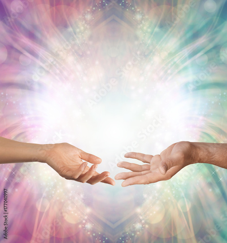 Male and Female energy merging - a female hand and a male hand with open palms facing each other against a beautiful intricate masculine and feminine colored energy background with copy space above 