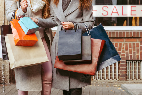 two girls with shopping bags in front of showwindow with sale writting on it