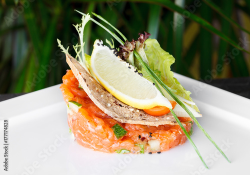 Fresh tartare with salmon and cucumber on a white plate, close up
