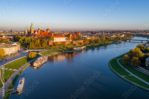 Skyline panorama of Cracow, Poland, with Royal Wawel Castle, Cathedral, Vistula River, bridge, harbor, ships and onboard restaurant. Aerial view in fall in sunset light.