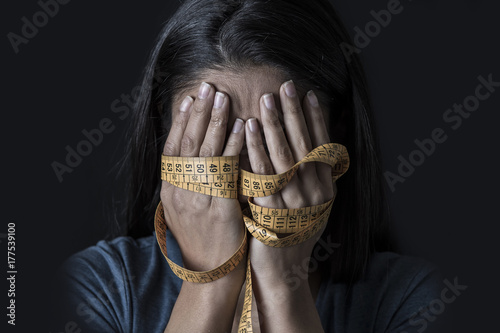 hands wrapped in tailor measure tape covering face of young depressed and worried girl suffering anorexia or bulimia nutrition disorder