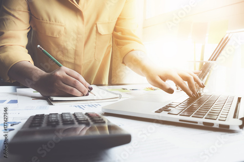 Close up of businesswoman or accountant hand holding pen working on calculator to calculate business data, accountancy document and laptop computer at office, business finance concept