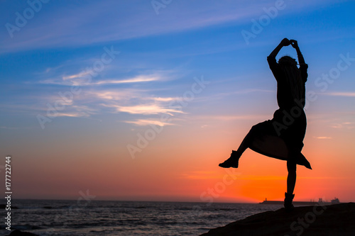 Silhouette of a young fun woman on the sea beach at amazing sunset.