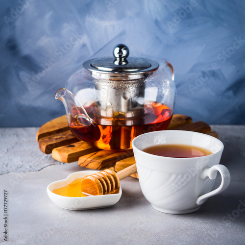 Cup of red tea rooibos and honey with glass teapot on blue