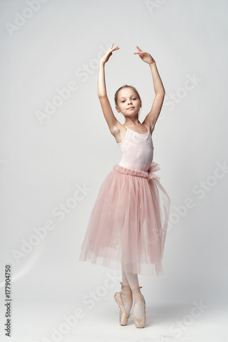 little ballerina in a light bundle and pointe poses with her arms raised