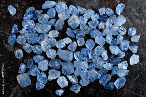 Collection of lovely blue rough and uncut sapphire gemstones on black stone slate.