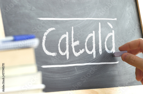 Hand writing on a blackboard in a language class with the word CATALAN wrote on. Some books and school materials.