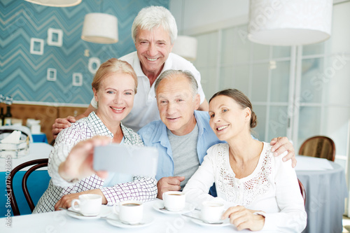 Smiling senior friends making selfie during their hangout in cafe