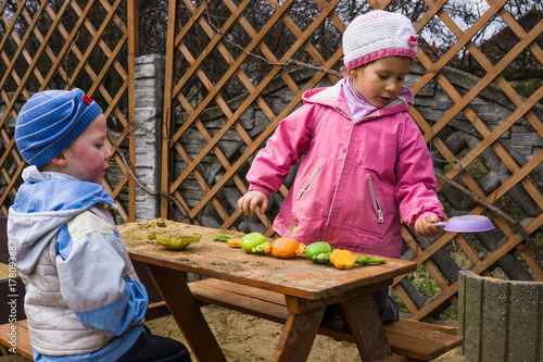 Dziewczynka i chłopiec bawią się piaskiem na ławce w przydomowym placu zabaw.
