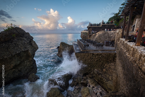 Bali, Indonesia - August 1, 2017: People eating in outdoor terrace during sunset at Coastline Of famous Rock Bar in Bali, Indonesia