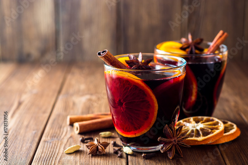 Two glasses of christmas mulled wine with oranges and spices on wooden background.