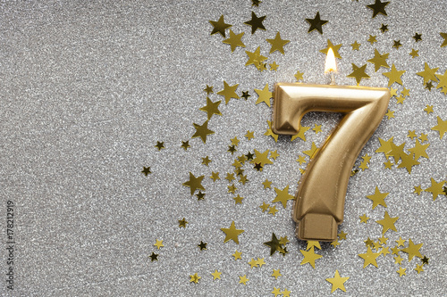 Number 7 gold celebration candle on star and glitter background