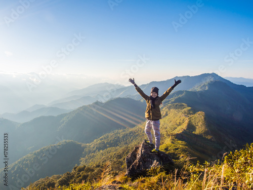 The best happy moment of a cute girl finished her first trekking. Look how happy she is after she saw this great green nature view of mountain ridge range with the orange morning sky of sunrise
