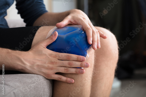 Person Sitting And Applying Ice Gel Pack On Knee