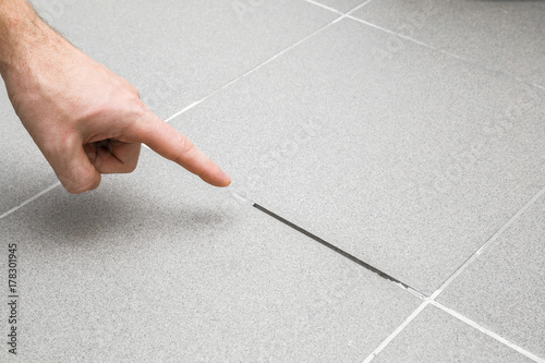 Man's hand finger pointing to space between tiles. Damaged tiles seam. Building problem concept.