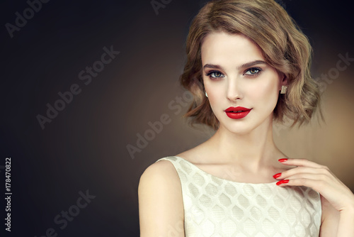 Beautiful model girl with short curly hair and red lips . Red manicure on nails .Beauty and esthetic care 