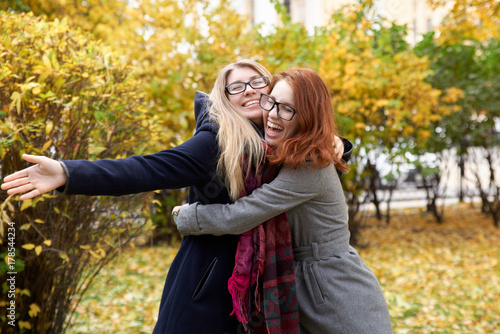 two young friend women to get together and hug each other with a big smile and joyful mood on a background of autumn Park and orange leaves
