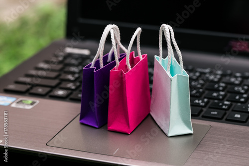 Three colorful paper shopping bags on laptop keyboard. Ideas about online shopping. e-commerce or electronic commerce is a transaction of buying or selling goods or services online over the internet.