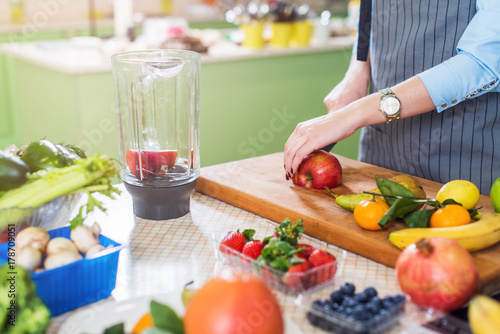 Cropped image of female cook cutting fruit on board preparing smoothie in kitchen