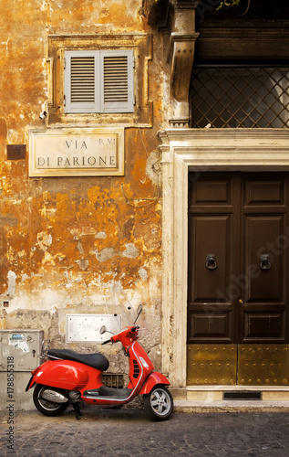 Narrow street in Rome with a typical red vespa scooter on a cobblestone street