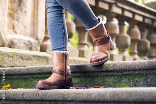 A stylish girl wearing leather boots walking on historic stone stairs, fashion concept 