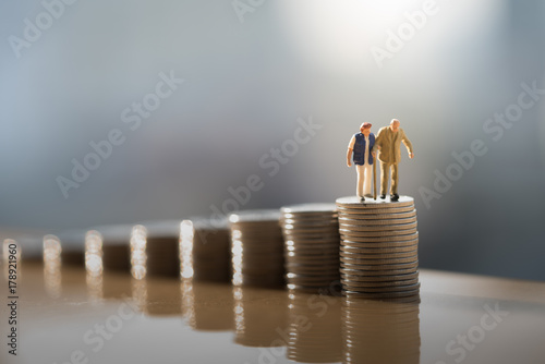 Concept of retirement planning. Miniature people: Old couple figure standing on top of coin stack.