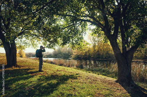 Man is watching birds with binoculars by the river in autumn.