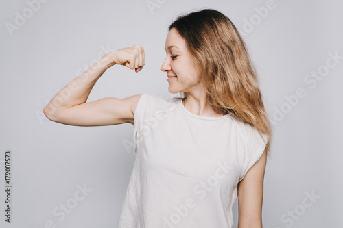 confident young sporty Caucasian woman in a white t-shirt showing biceps against white background