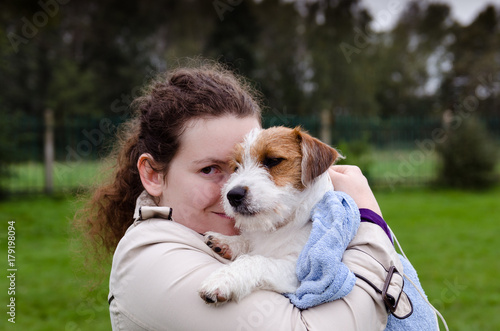 Szczeniak Jack Russell terrier na rękach swojej właścicielki. Zdjęcie w plenerze w wietrzny deszczowy jesienny dzień.