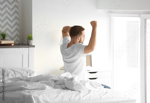 Morning of handsome young man sitting on bed at home