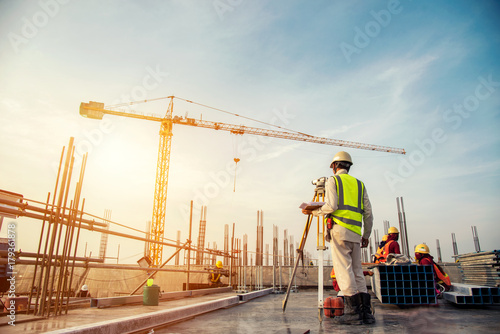 Surveyor builder Engineer with theodolite transit equipment at construction site outdoors during surveying work