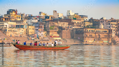 Varanasi city with old architectural buildings and ancient temples with tourists boat along the Ganges river ghat.