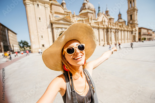 Young woman tourist making selfie photo in front of the famous cathedral on the central square during the sunny weather in Zaragoza city, Spain