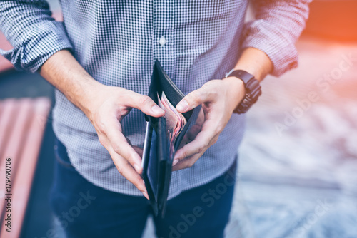 Man standing holding black wallet full of money