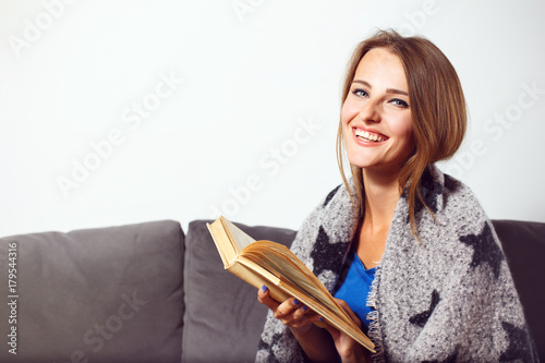 Cheerful girl sitting in armchair with plaid and glass of tea before bricks wall