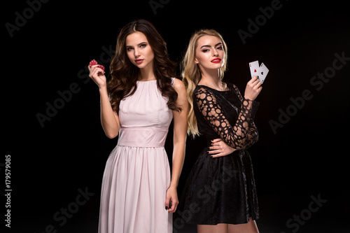 Two Sexy girls brunette and blonde, posing with chips in her hands, poker concept black background