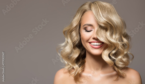 Blonde woman with curly beautiful hair smiling on gray background.