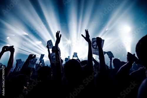 silhouettes of concert crowd in front of bright stage lights. pacifism sign on paper