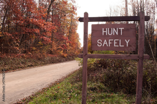 A "HUNT SAFELY" sign on the side of a dirt road in the fall woods