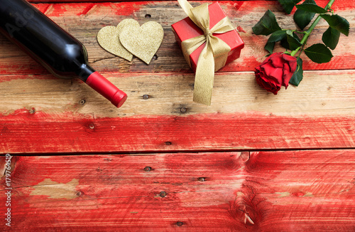 Valentines day. Red wine bottle, rose and a gift on wooden background
