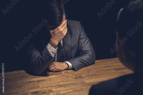 Suspect businessman displaying regret in dark interrogation room