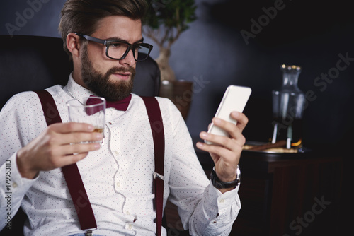 Businessman using his smartphone and drinking tea .