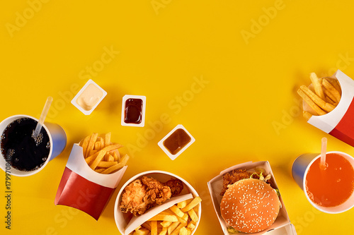 Fast food concept with greasy fried restaurant take out as onion rings, burger, fried chicken and french fries as a symbol of diet temptation resulting in unhealthy nutrition.