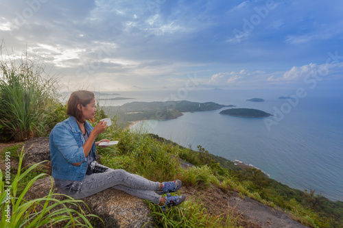 a lady drinking coffee on the highest viewpoint name Pha Hin Dum. on Pha Hin Dum viewpoint can see around Phuket island. Niharn beach wind turbine Phomphep cape Rawai beach are in front of Pha Hin Dum