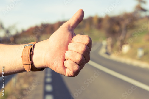 Male hitchhiker holding thumbup on the side of the road