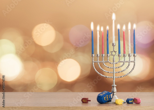 Hanukkah Jewish holiday background with menorah (Judaism candelabra) burning candles and traditional Dreidrel game toy on wood table and on autumn bokeh sun flare