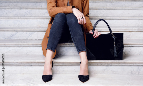 Fashion woman sit in high heels shoes hold black big bag
