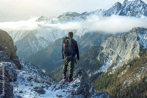 Man hiker with backpack on top of the mountain back, looking at the snow slope. Concept motivation and goal achievement