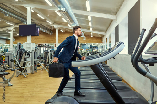 A businessman is running on a treadmill in the gym.